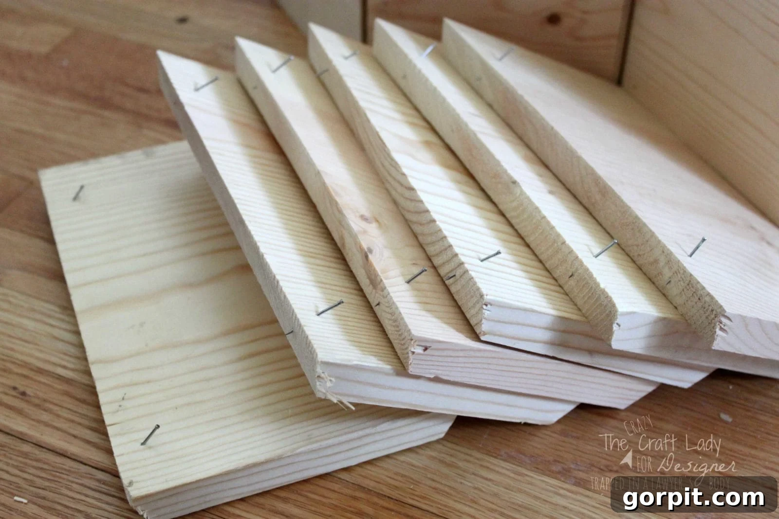 Honeycomb Shoe Rack DIY 10 A stack of pre-cut wooden boards with nails partially inserted, prepared for assembly on a hardwood floor. These pieces will be transformed into hexagonal shoe cubbies for a DIY shoe rack.