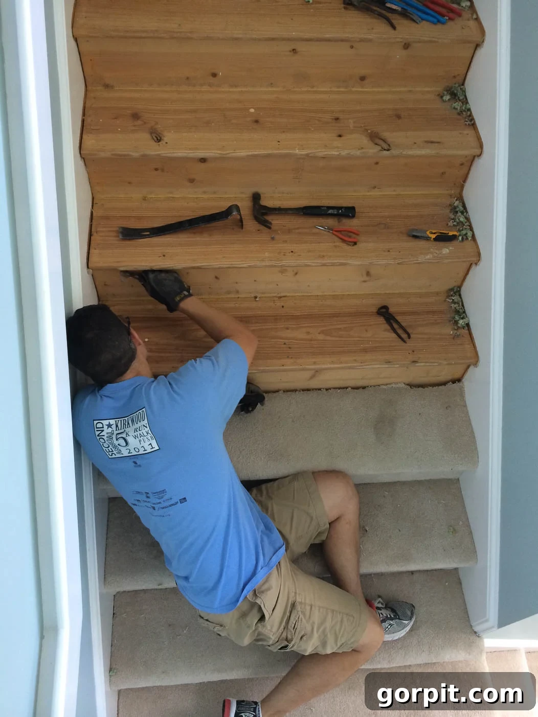 Person ripping off old beige carpet from stairs to prepare for DIY hardwood treads installation.