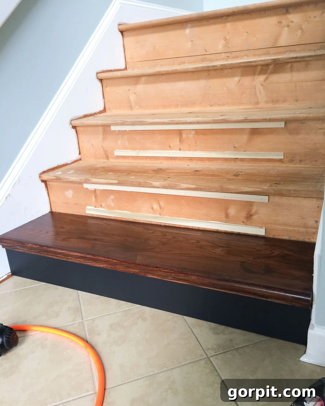 Installing the first DIY hardwood stair tread and riser, showing shim placement for proper alignment.