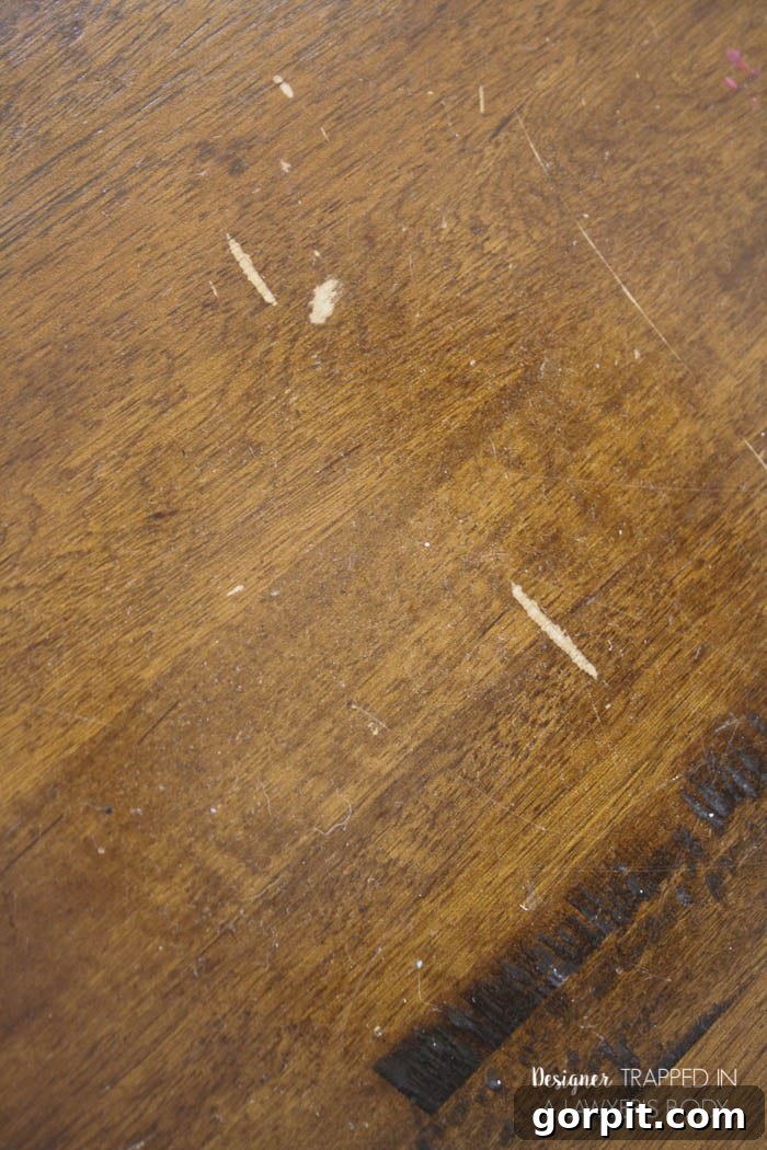 Close-up of a scratched wood tabletop, highlighting deep imperfections and dull finish.