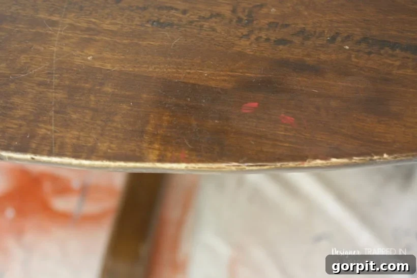 Detail of a damaged table edge, showing exposed wood and loss of original finish.