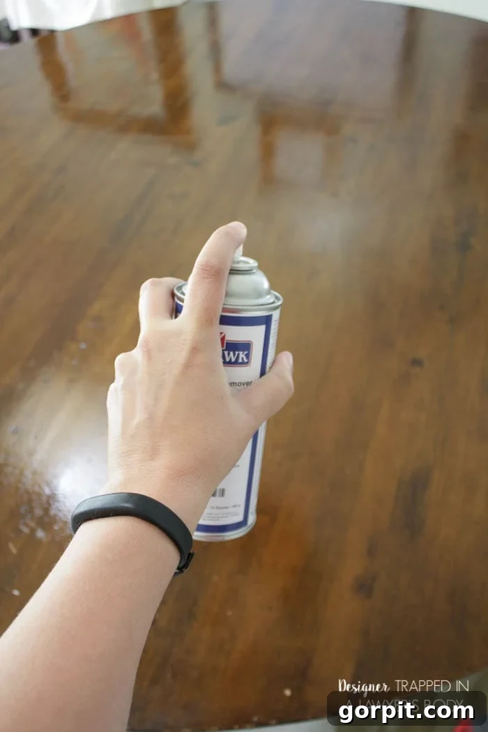 Spraying Mohawk Wax Wash Remover on a wooden table to clean the surface.