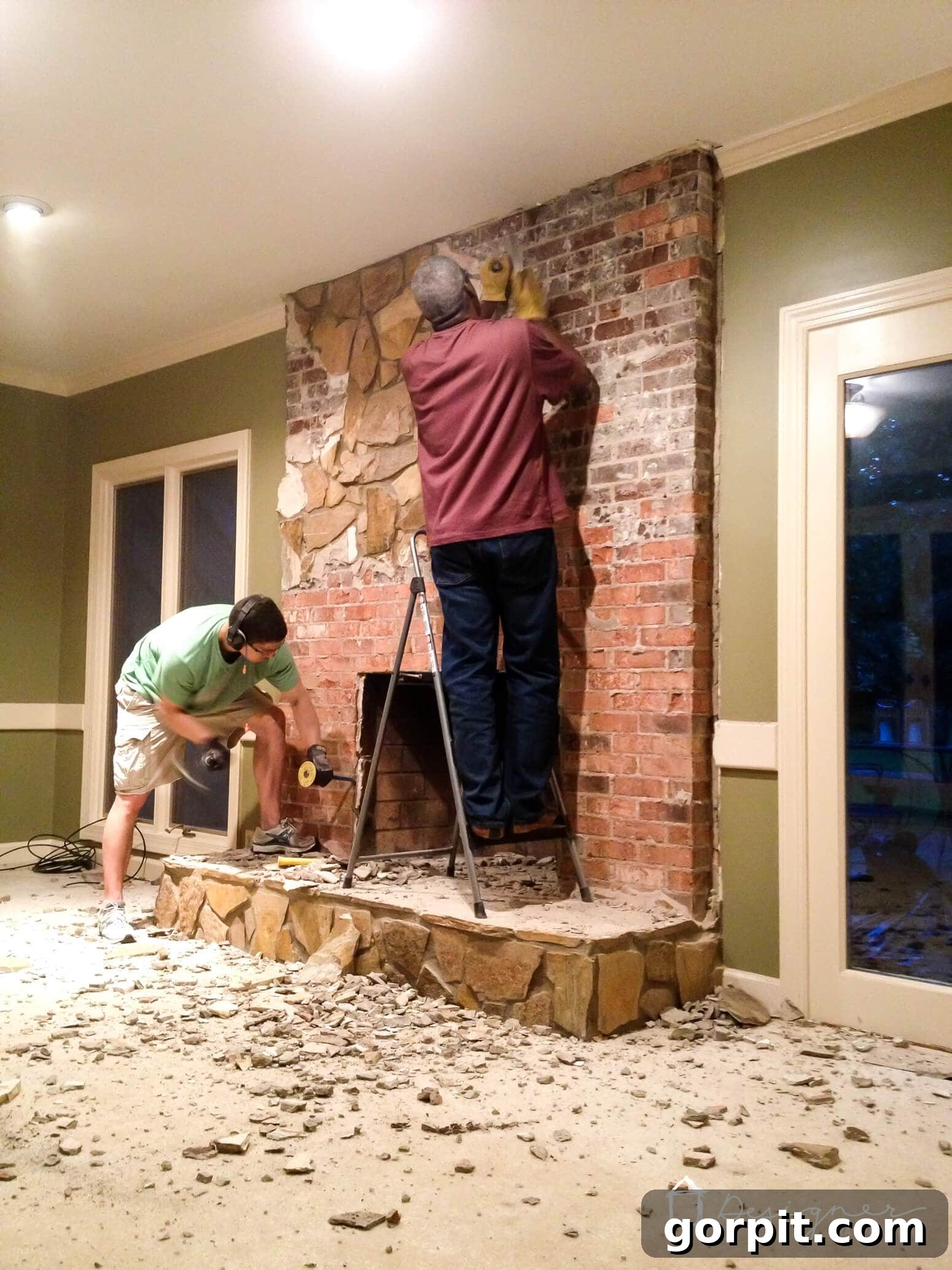 Demolishing an old stone fireplace facade to reveal the brick underneath, a crucial step for a DIY concrete makeover.
