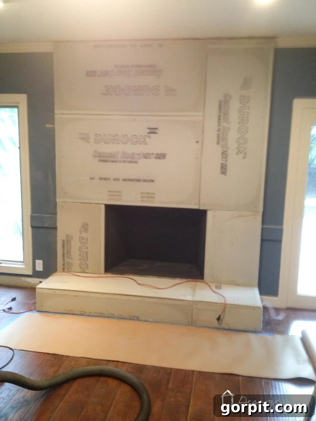 Attaching cement board to a brick fireplace using an electric drill and masonry screws, with mesh tape reinforcing seams.