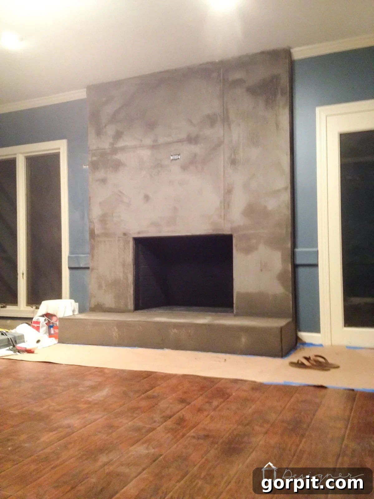 First thin coat of concrete applied to a DIY fireplace, showing visible cement board seams while drying.